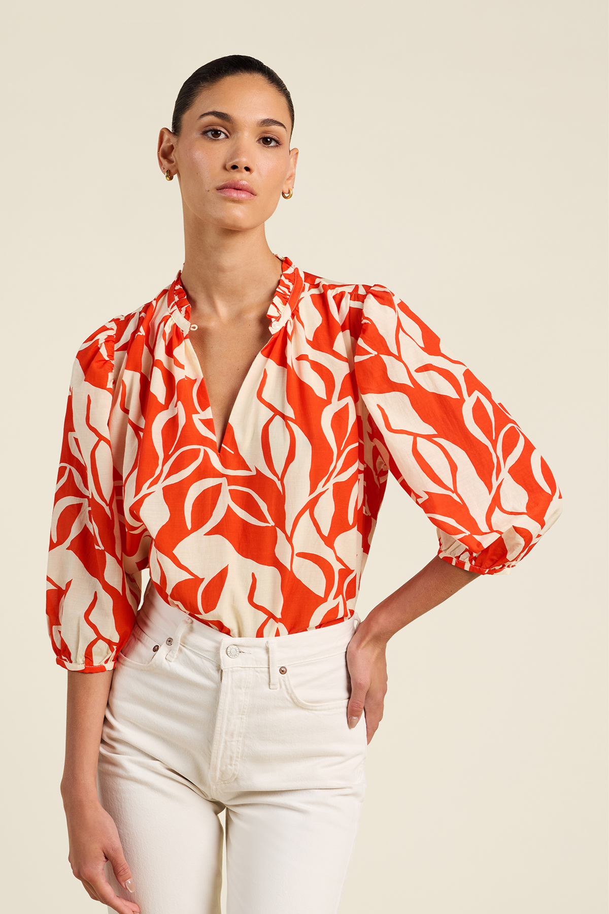 Woman wearing a red and white patterned blouse with white pants on a beige background