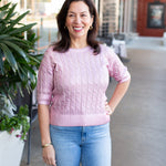 Woman wearing a pink sweater and blue jeans standing outdoors.
