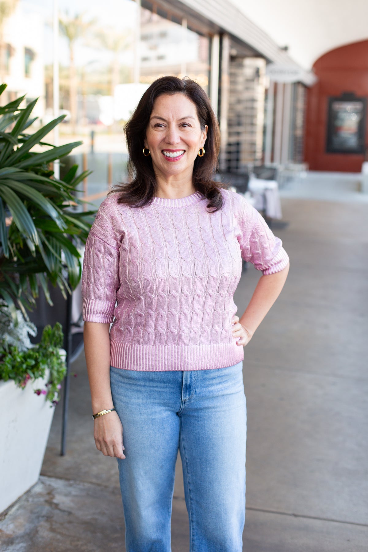 Woman wearing a pink sweater and blue jeans standing outdoors.