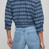 Person wearing a blue patterned jacket and light blue jeans on a gray background