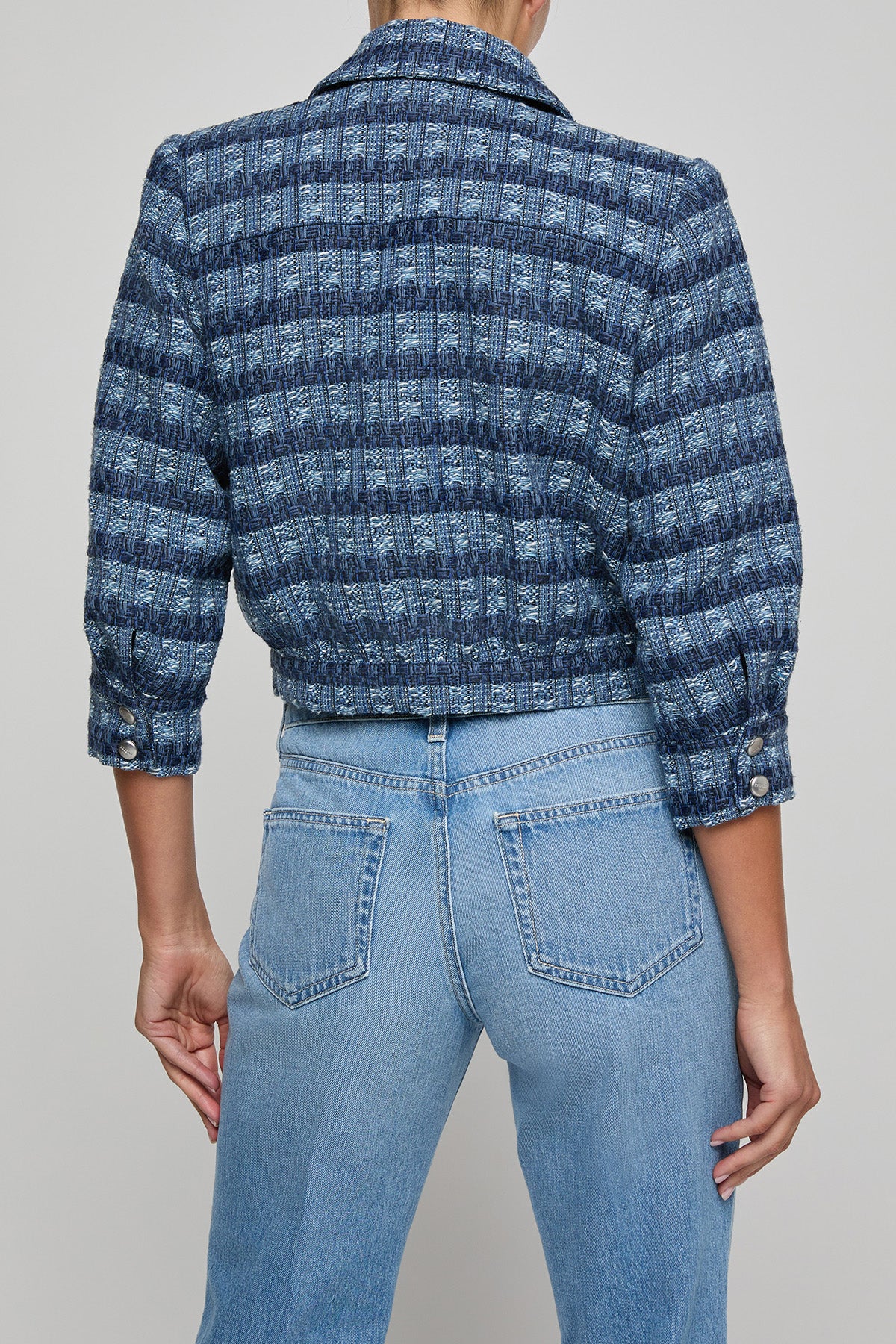 Person wearing a blue patterned jacket and light blue jeans on a gray background