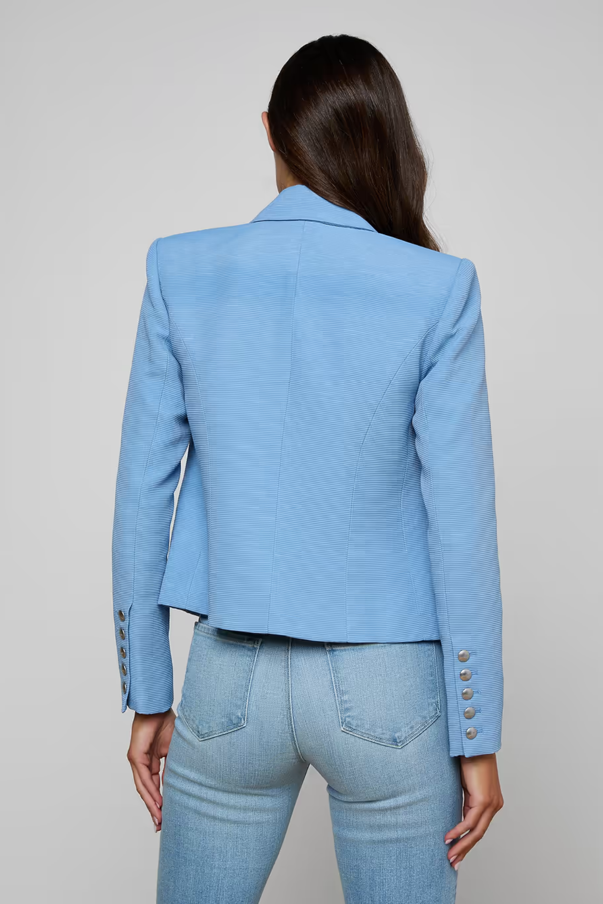 Person wearing a light blue blazer and jeans on a plain background