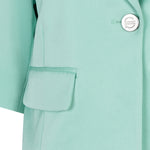 Close-up of a light green coat with a button and pocket detail.