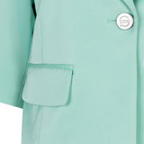 Close-up of a light green coat with a button and pocket detail.