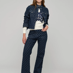 A model stands against a light gray studio background wearing a matching navy blue patterned jacket and wide-leg pants set with a white top.