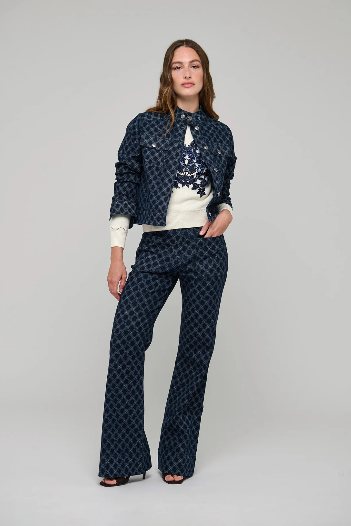 A model stands against a light gray studio background wearing a matching navy blue patterned jacket and wide-leg pants set with a white top.