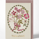 A floral greeting card with a striped cream background, an oval bouquet illustration in pink, green, and beige tones, and the text 'Thanks a bunch!' at the bottom, shown with a mauve envelope behind it on a light gray background.