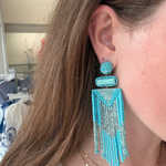 A close-up of a woman wearing a large turquoise and silver beaded dangle earring, with her ear, hair, and neck visible.
