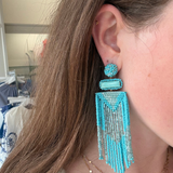 A close-up of a woman wearing a large turquoise and silver beaded dangle earring, with her ear, hair, and neck visible.