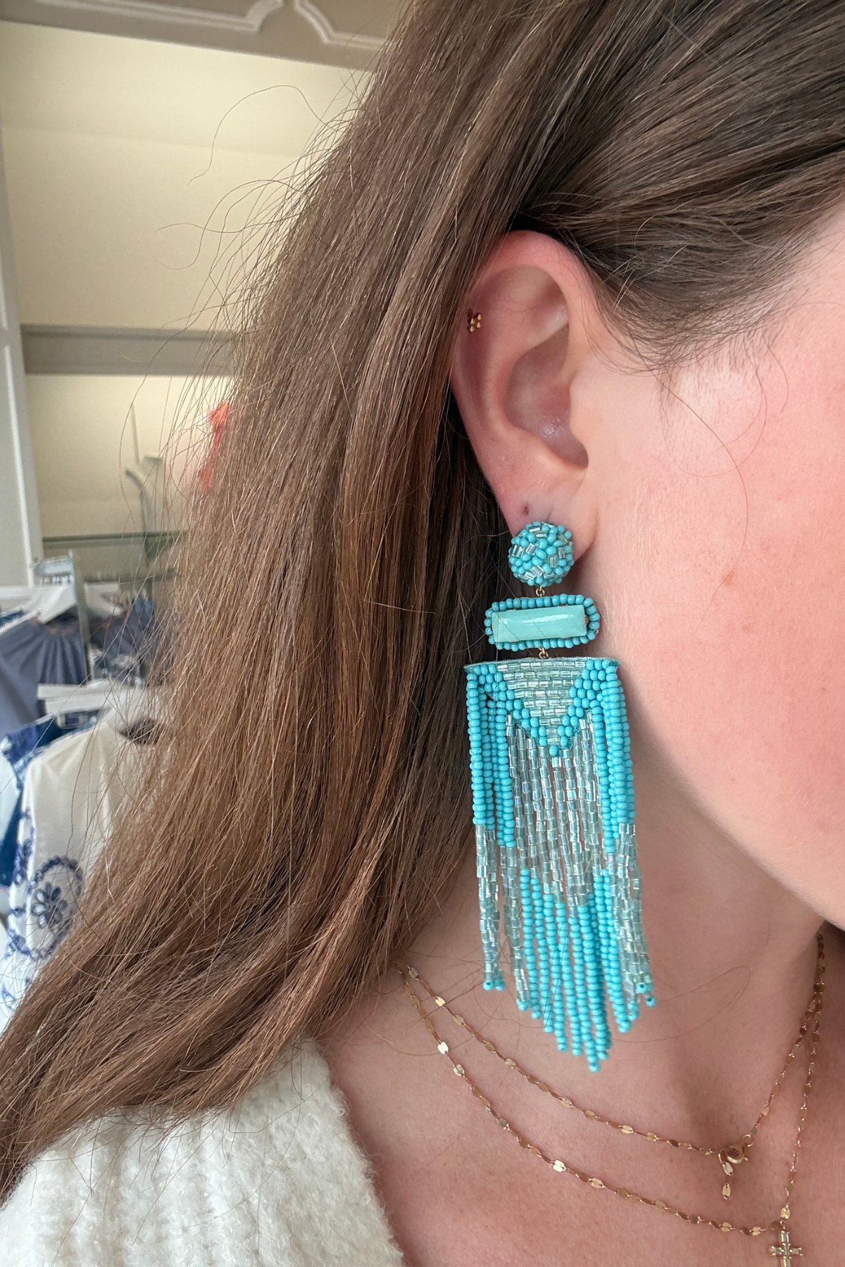 A close-up of a woman wearing a large turquoise and silver beaded dangle earring, with her ear, hair, and neck visible.