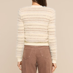A woman shown from the back wearing a cream-colored textured knit sweater with horizontal striped patterns and brown wide-leg pants, set against a solid beige studio background.