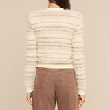 A woman shown from the back wearing a cream-colored textured knit sweater with horizontal striped patterns and brown wide-leg pants, set against a solid beige studio background.