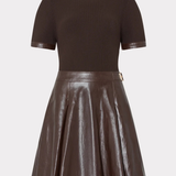 A dark brown two-piece outfit featuring a short-sleeve ribbed knit top and a matching faux-leather pleated skirt with a small gold-tone belt buckle, shown on a light gray background.
