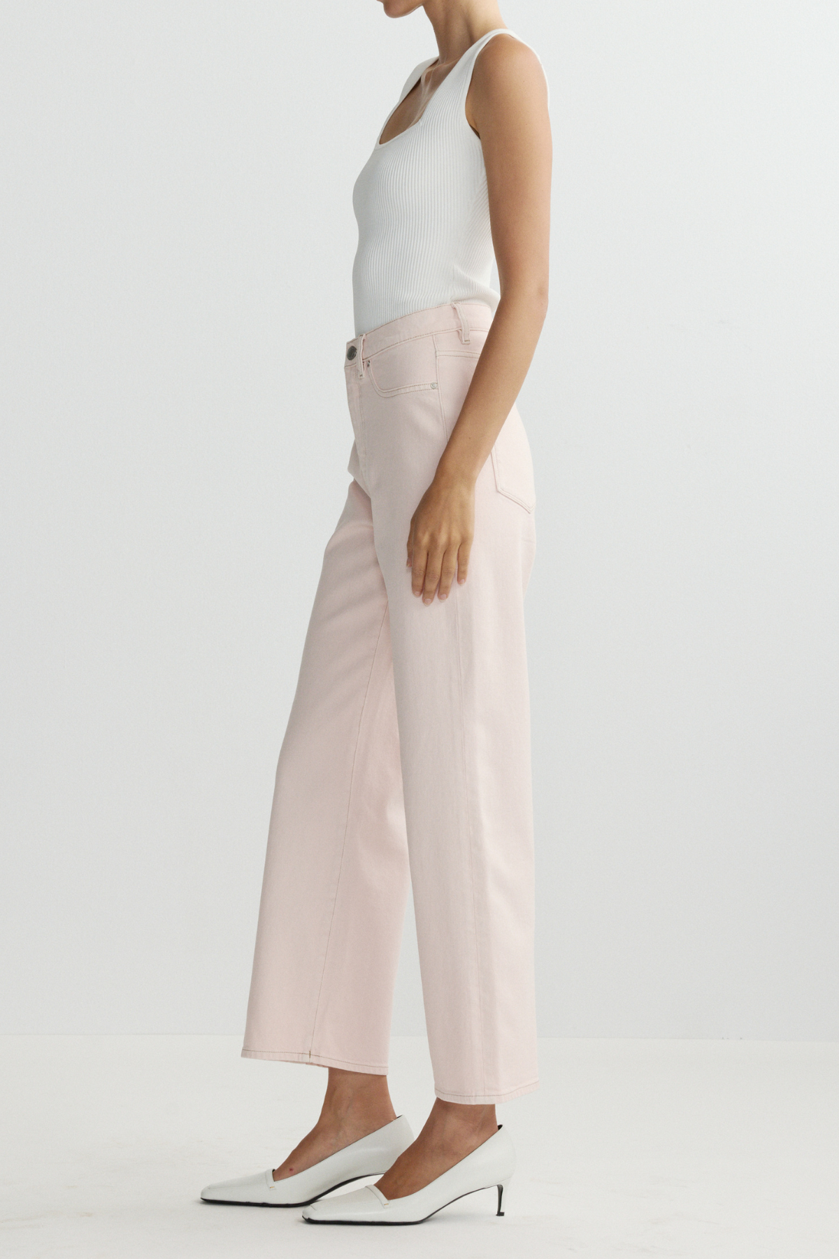 Person wearing a white tank top and light pink pants on a plain background