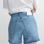 Person wearing blue denim shorts and a white top on a plain background