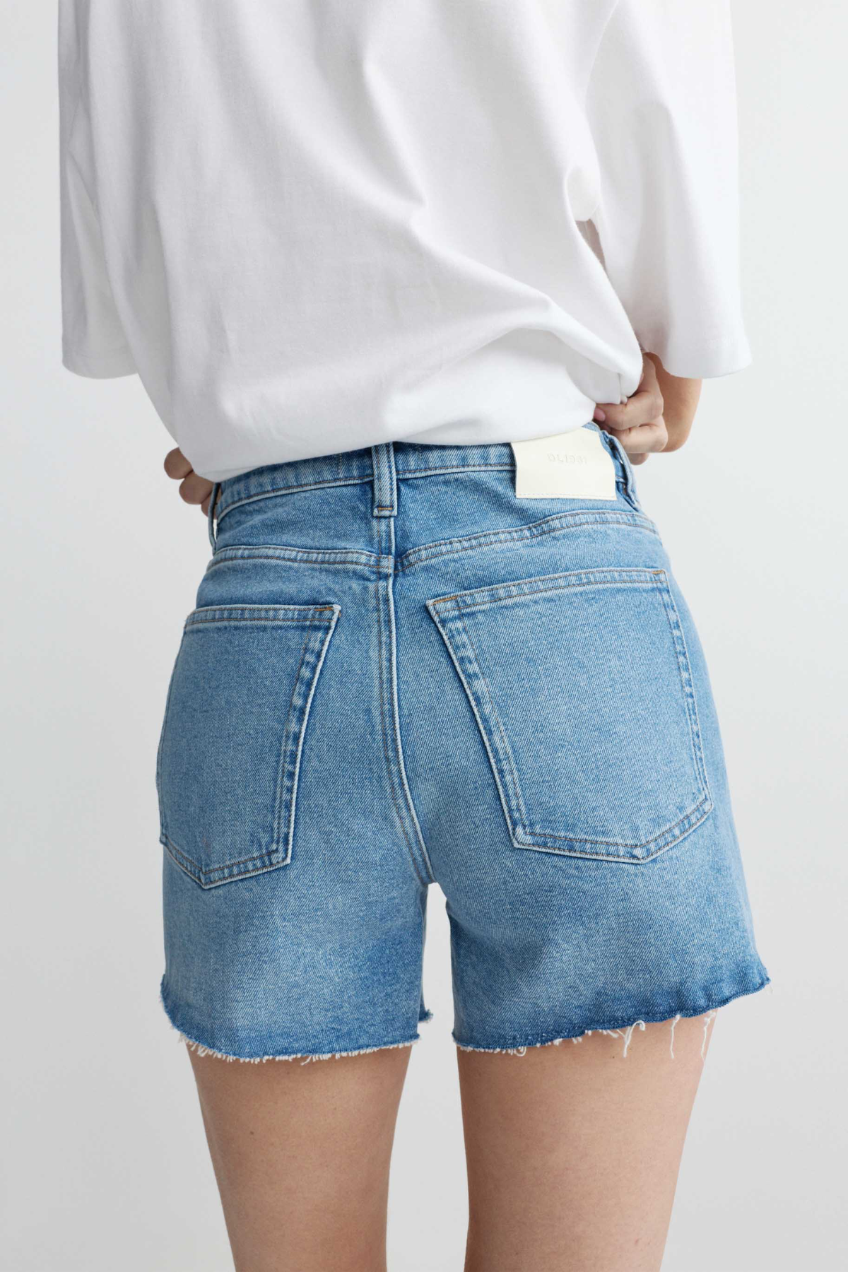 Person wearing blue denim shorts and a white top on a plain background