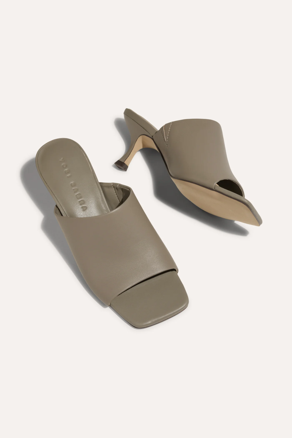 Pair of beige high-heeled mules on a light gray background