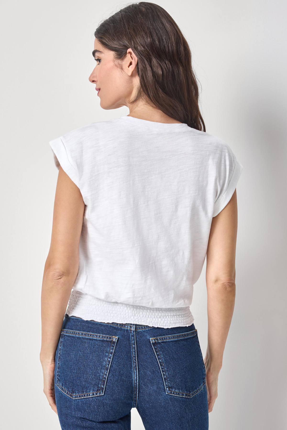 Woman wearing a white top and blue jeans against a plain background