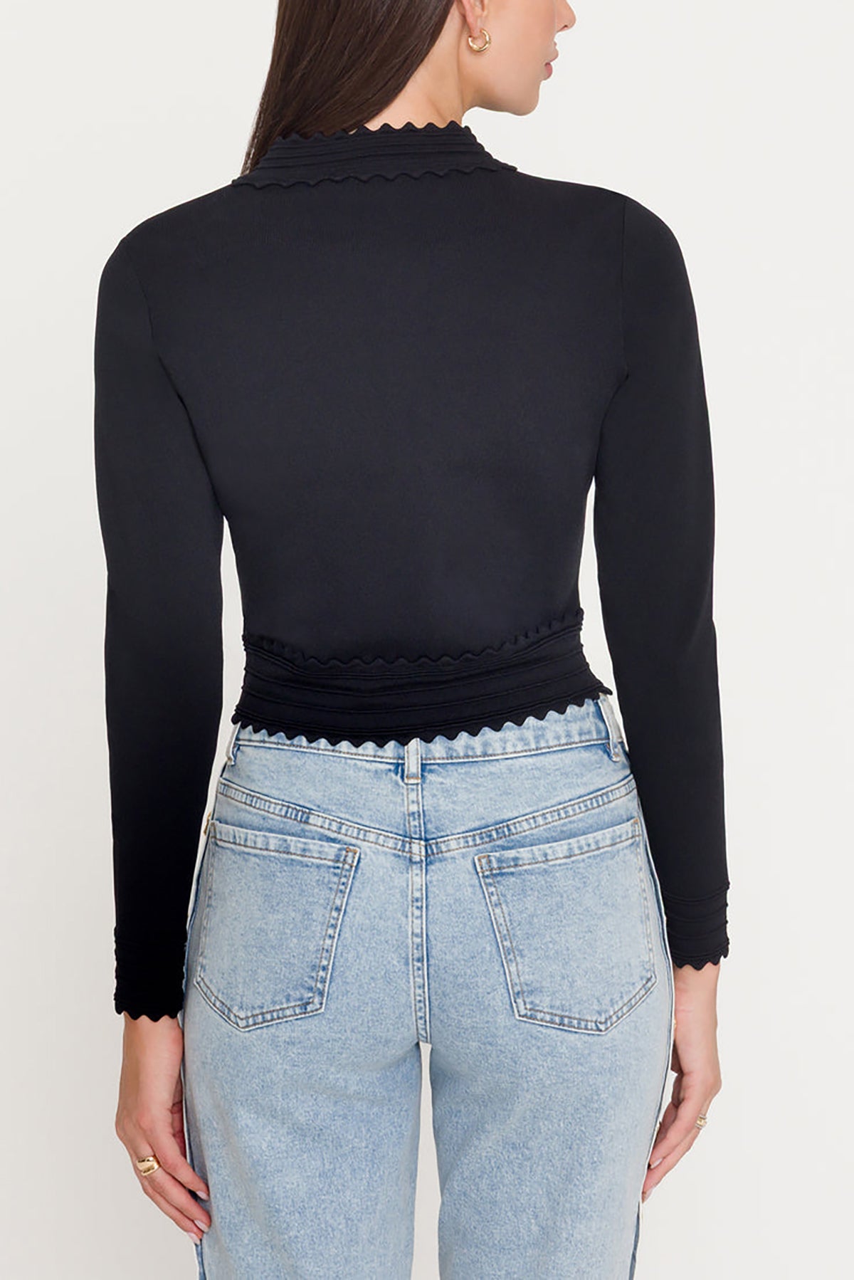 Person wearing a black long-sleeve top and light blue jeans on a white background