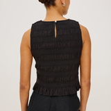Woman wearing a black sleeveless top with pleated details on a white background