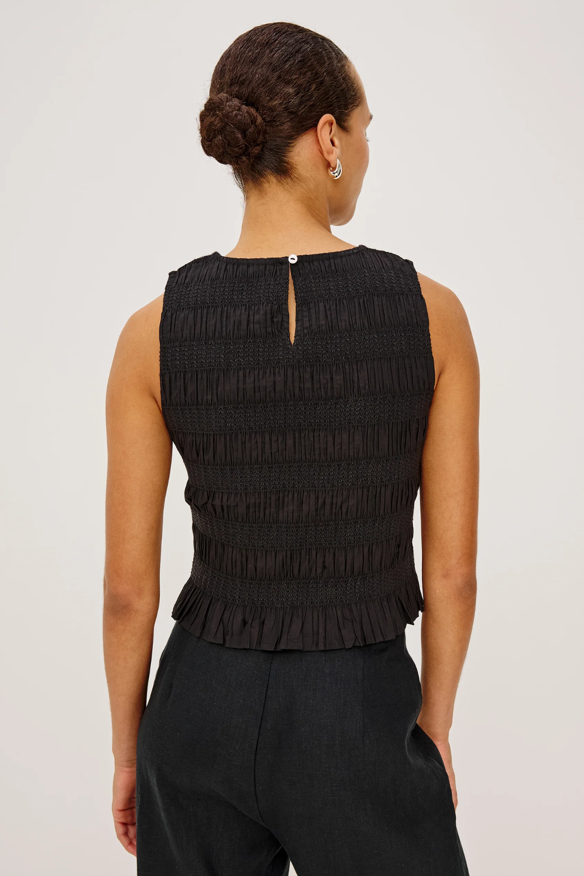 Woman wearing a black sleeveless top with pleated details on a white background