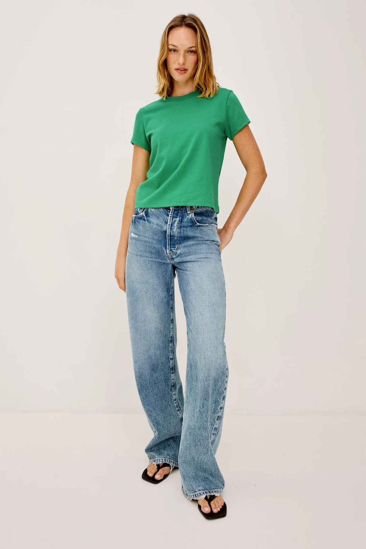 Woman wearing a green t-shirt and blue jeans on a white background
