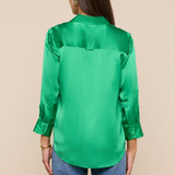 Woman wearing a green satin blouse and blue jeans on a beige background