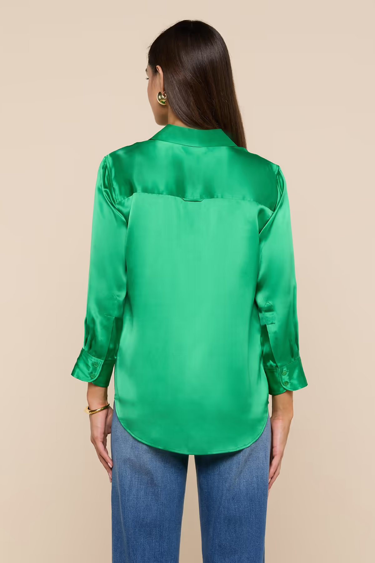Woman wearing a green satin blouse and blue jeans on a beige background