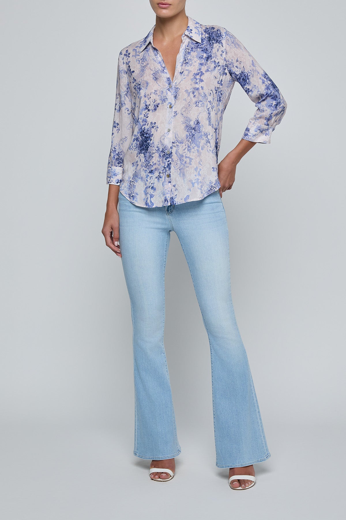 Woman wearing a floral blouse and light blue jeans on a gray background