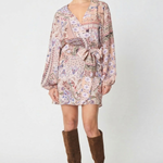 A model wearing a long-sleeved mini wrap dress with a pink and purple paisley pattern, styled with brown suede knee-high boots against a light gray studio background.