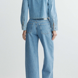 Person wearing a light blue denim jacket and jeans on a white background