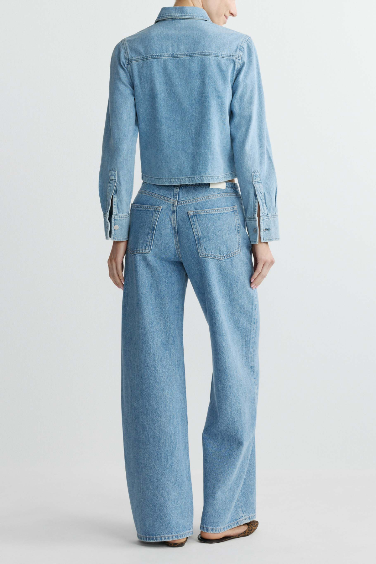 Person wearing a light blue denim jacket and jeans on a white background