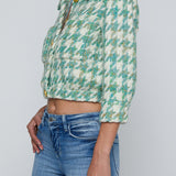 Person wearing a green and white patterned shirt and blue jeans on a light gray background