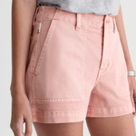A close-up of a model wearing light pink denim shorts with a gray t-shirt, cropped from the chest down against a light gray background.