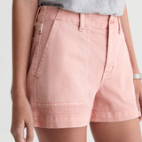 A close-up of a model wearing light pink denim shorts with a gray t-shirt, cropped from the chest down against a light gray background.