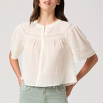 Woman wearing a white blouse with short sleeves and light green pants on a plain background