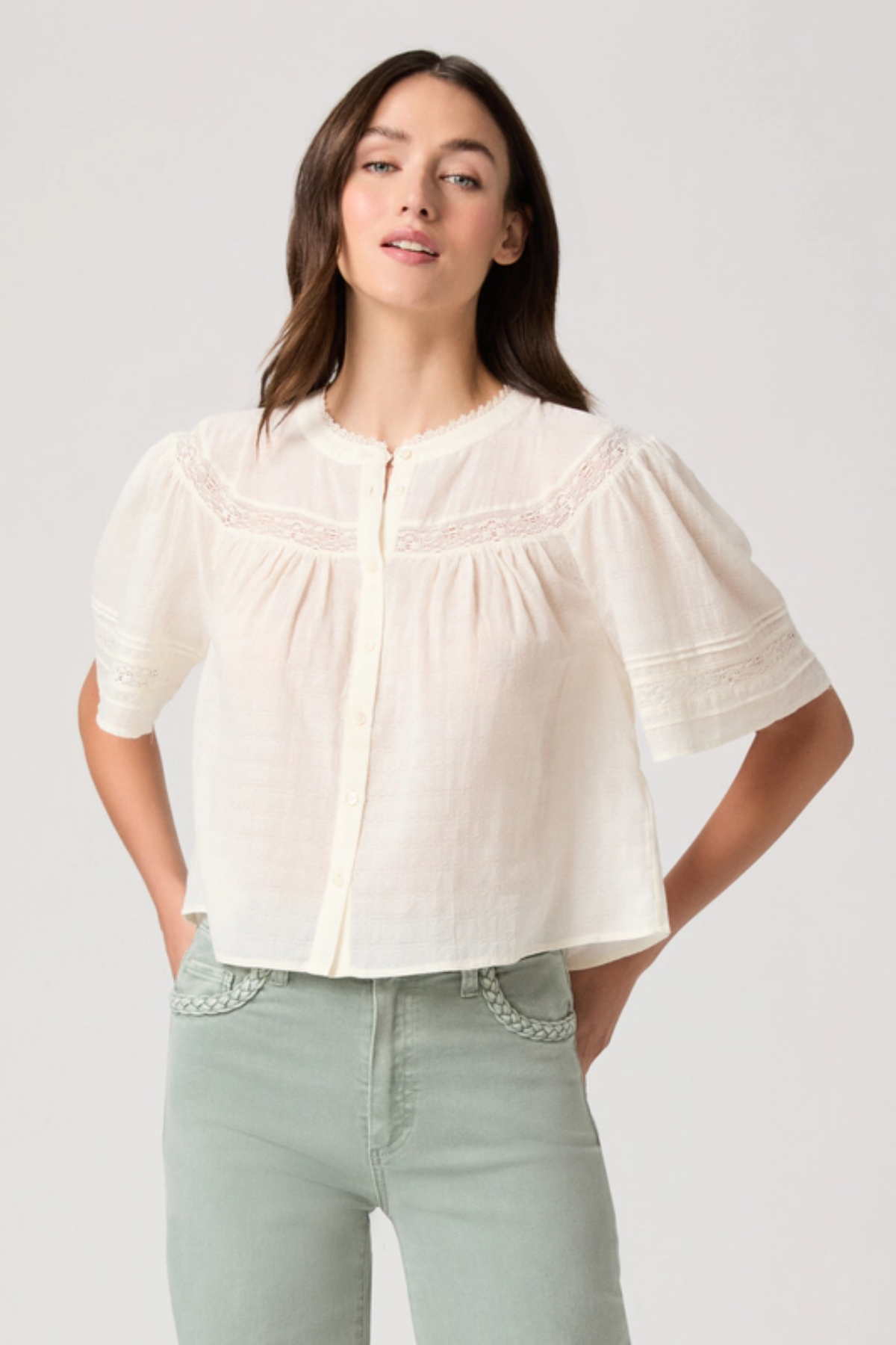 Woman wearing a white blouse with short sleeves and light green pants on a plain background
