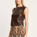 A woman modeling a sleeveless dark brown faux-leather top paired with a brown, beige, and pink patterned skirt, set against a plain light gray studio background.