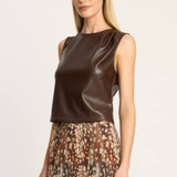A woman modeling a sleeveless dark brown faux-leather top paired with a brown, beige, and pink patterned skirt, set against a plain light gray studio background.