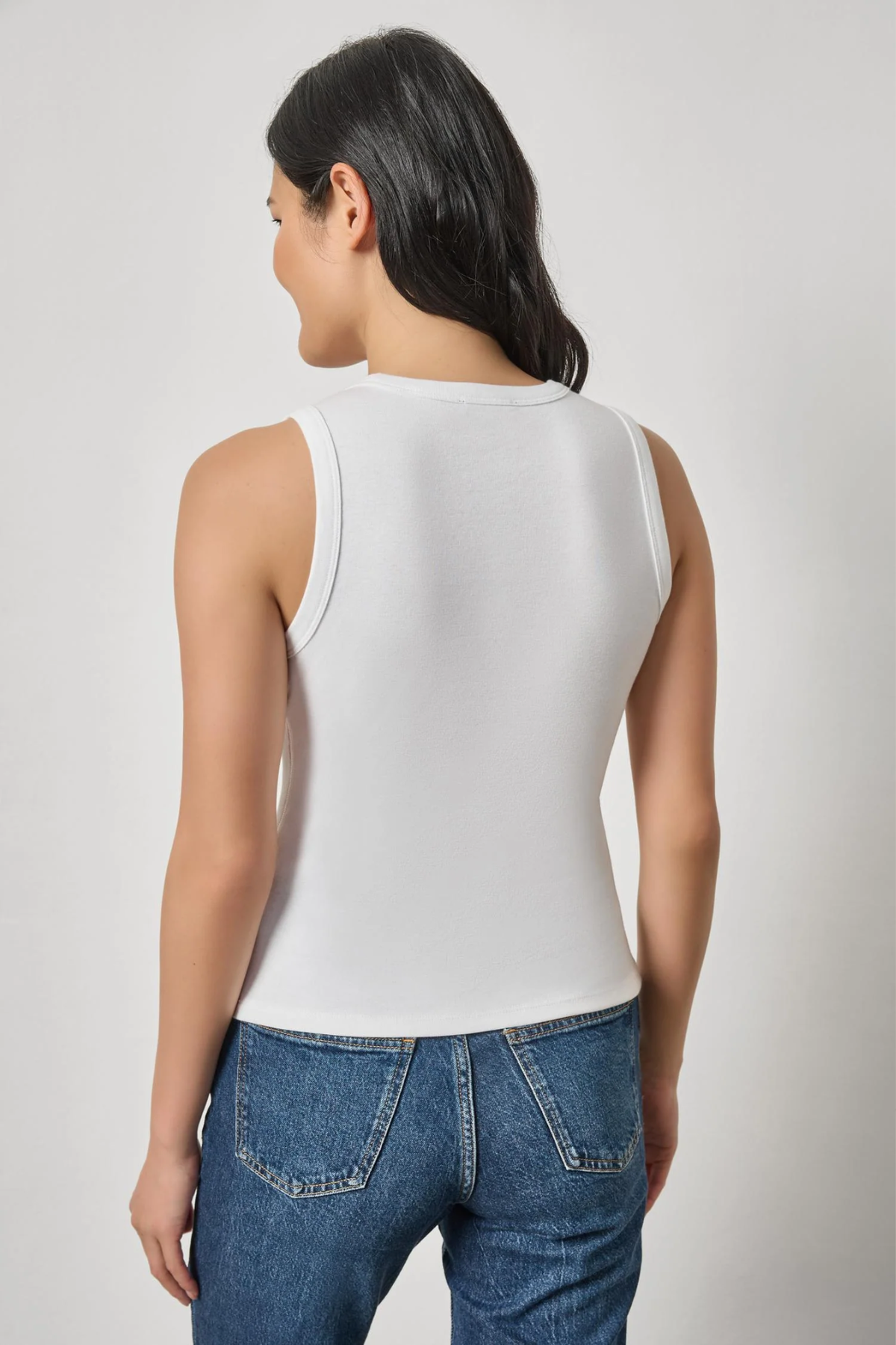 Model wearing a white sleeveless V-neck knit tank with blue denim.