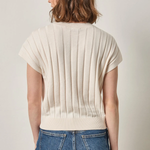 Person wearing a beige ribbed sweater and blue jeans on a plain background