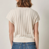 Person wearing a beige ribbed sweater and blue jeans on a plain background