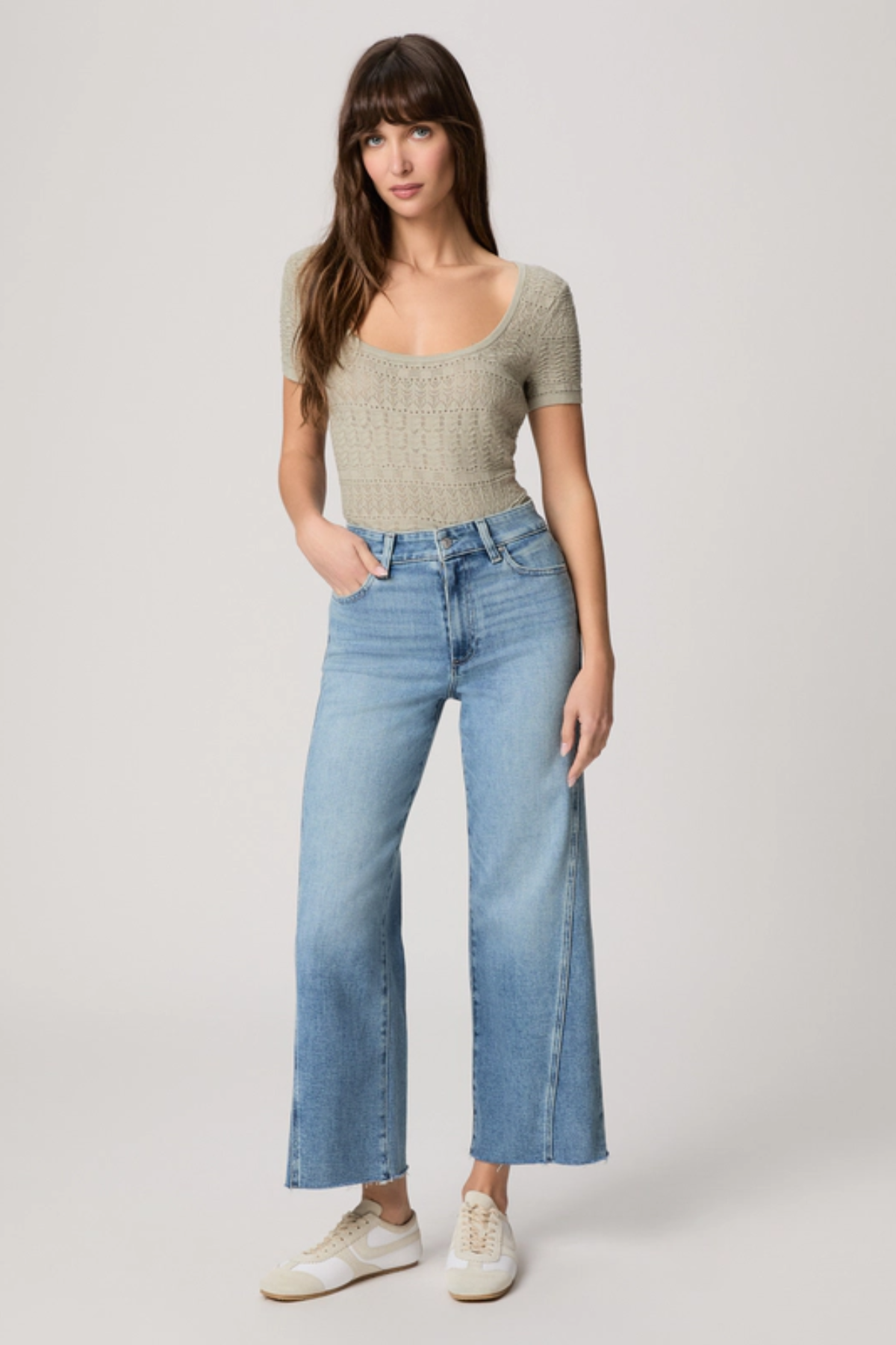 Woman wearing a beige top and light blue jeans on a white background