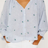 Person wearing a blue and white striped blouse with floral patterns on a plain background