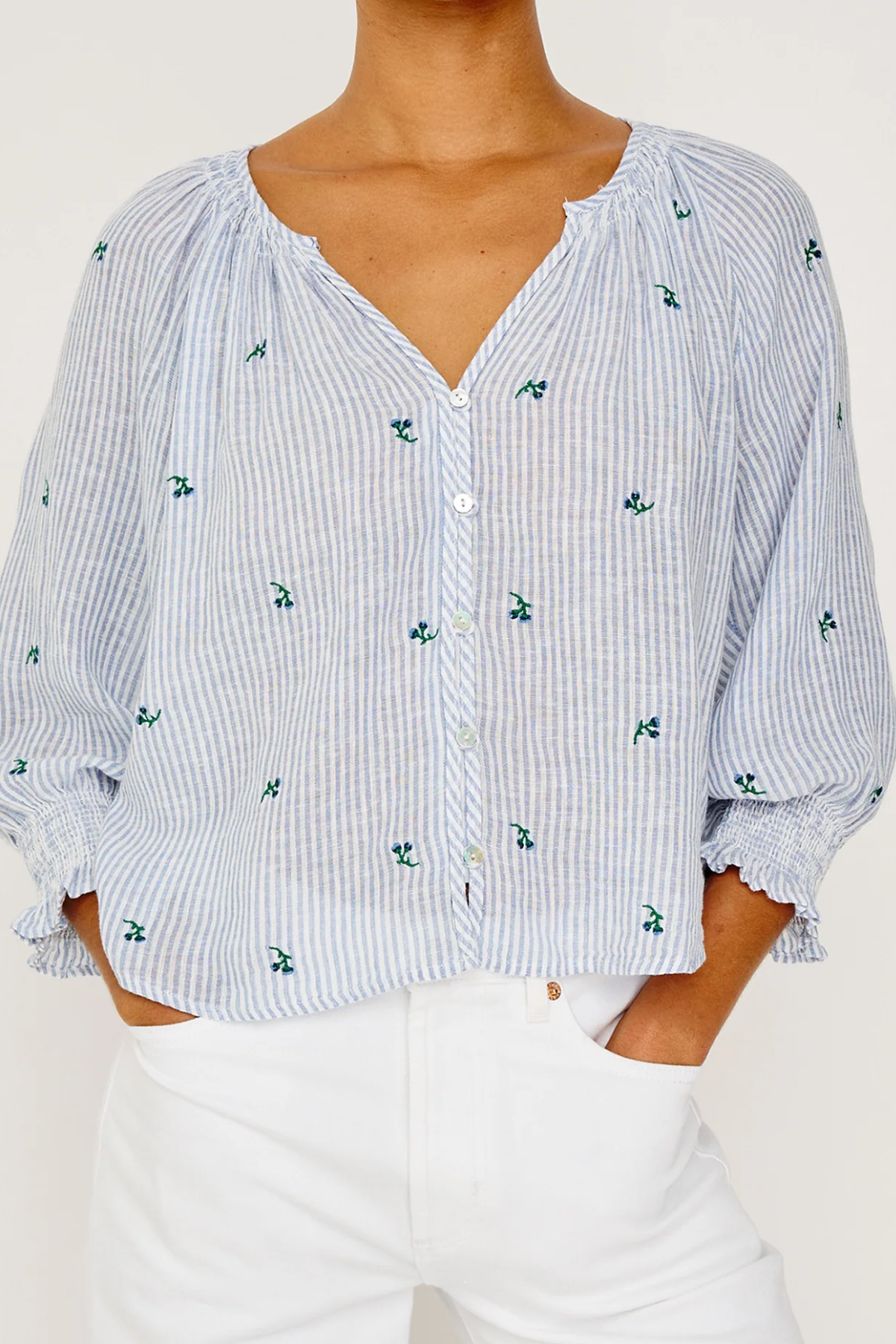 Person wearing a blue and white striped blouse with floral patterns on a plain background