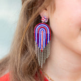 Close-up of a person wearing colorful beaded earrings with chains.