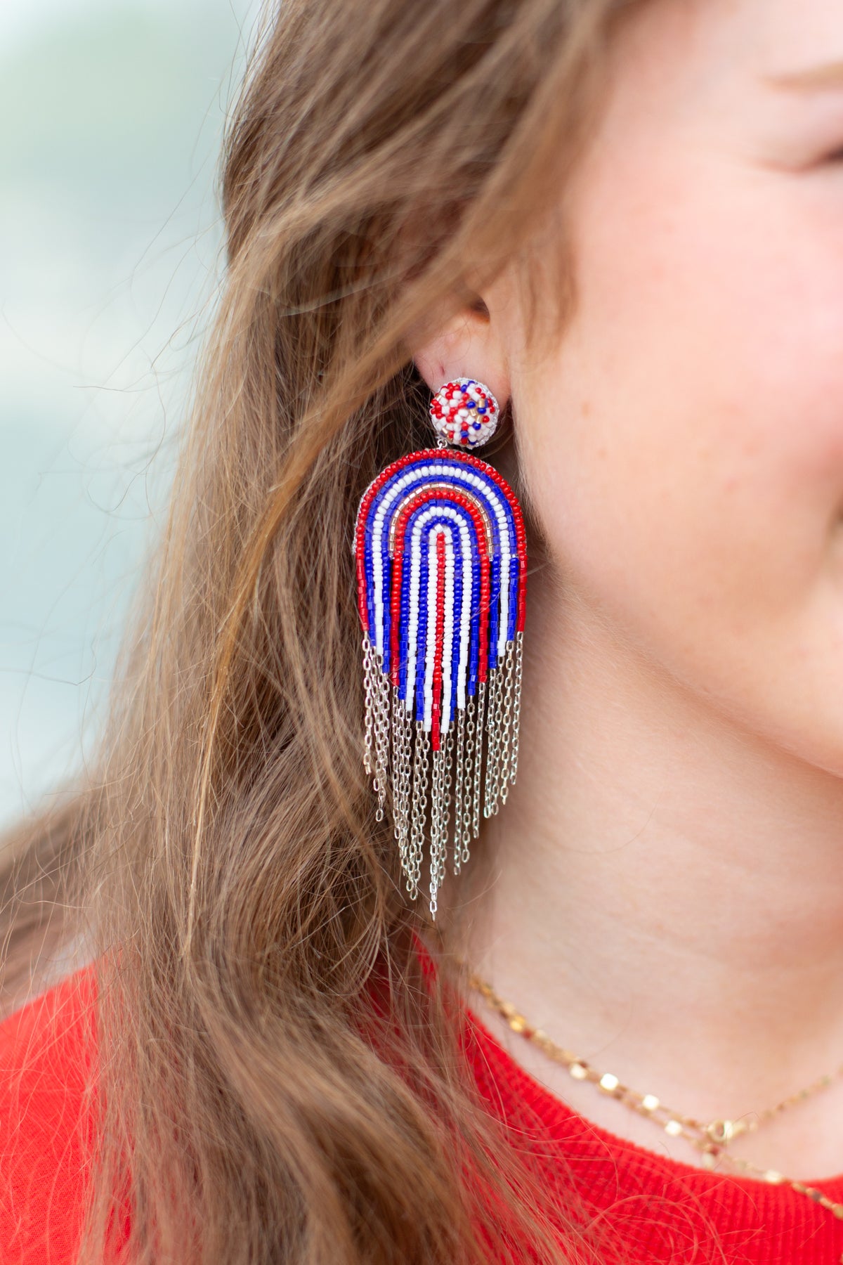 Close-up of a person wearing colorful beaded earrings with chains.