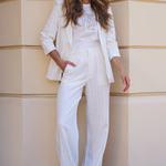 Woman in a white outfit standing against a beige wall.