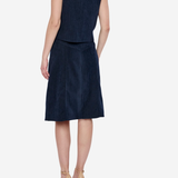 A woman shown from the back wearing a sleeveless navy blue dress with gold stud detailing around the neckline, paired with beige high-heeled sandals, against a light gray studio background.