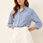 Woman wearing a blue and white striped shirt and white shorts on a beige background